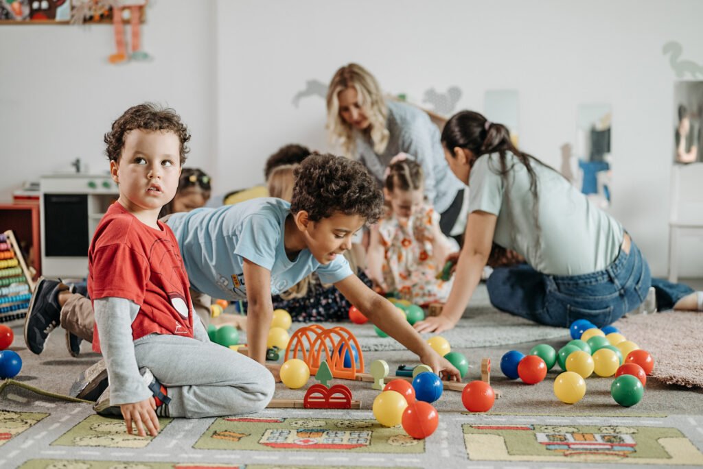 A friendly childcare center with caregivers interacting with happy children in a colorful playroom